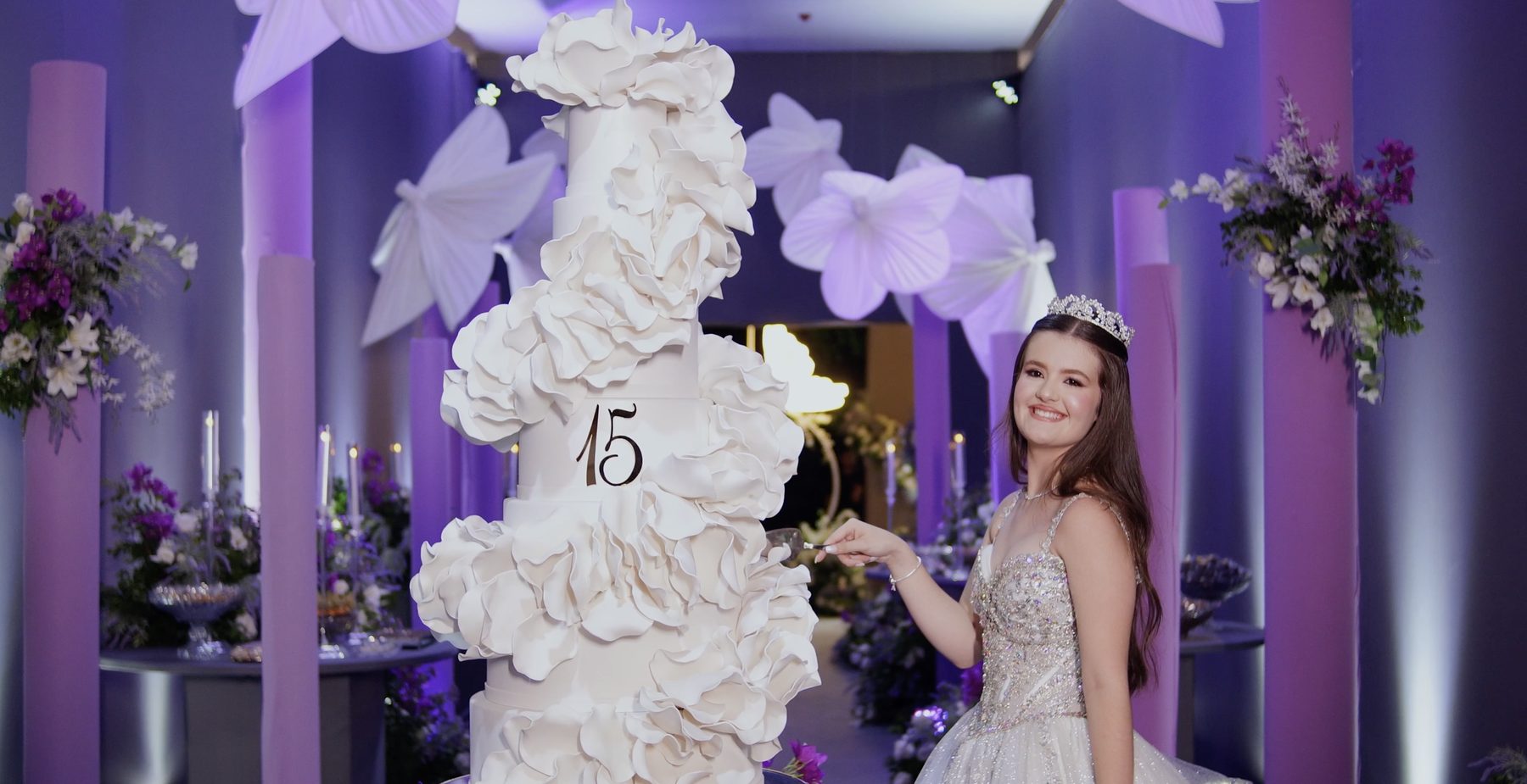 Debutante de coroa ao lado de um grande bolo branco com o número 15