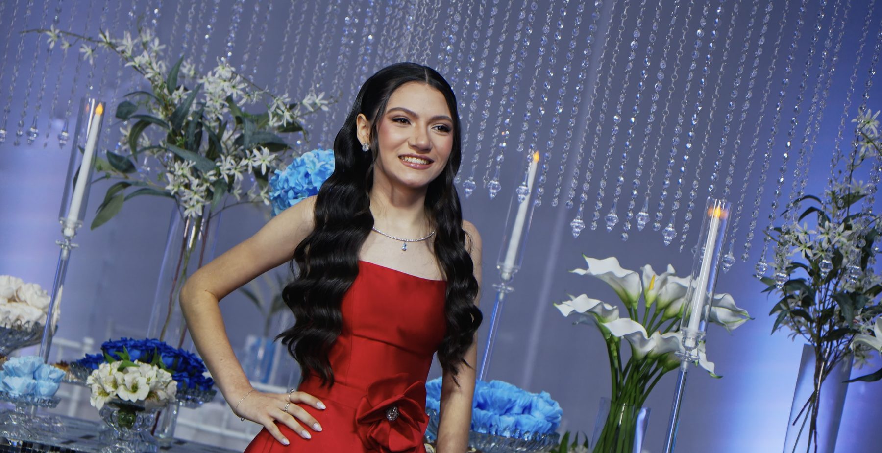 Debutante de vestido vermelho sorrindo diante de cortinas de cristais